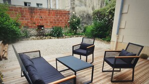 An outdoor patio with a wooden deck, a black sofa, two black chairs, and a small table.