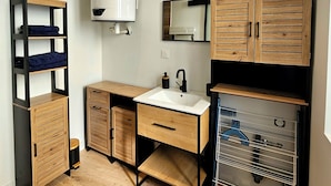 A compact, modern bathroom with a white sink, wooden cabinets, a mirror, and a built-in heater.