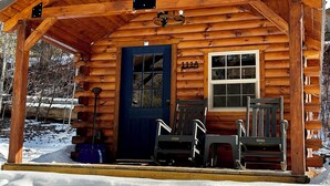 A log cabin with a porch, a blue door, and two rocking chairs.