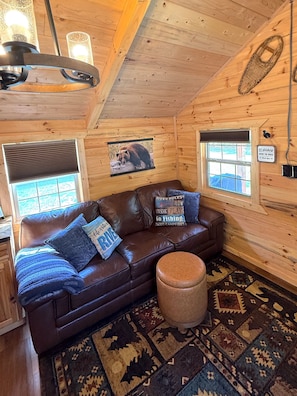 A cozy cabin interior with a brown leather sofa, patterned rug, and wooden walls.