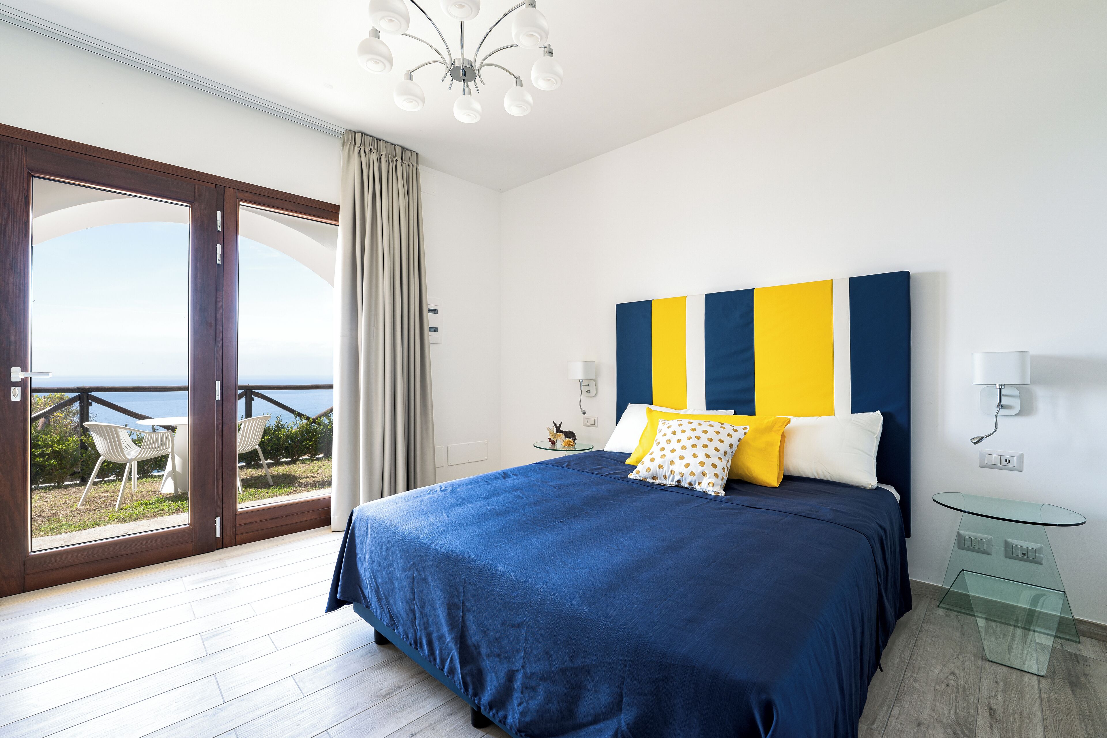 Ein Schlafzimmer mit einem großen Bett, einem Glastisch und Meerblick durch eine Schiebetür.