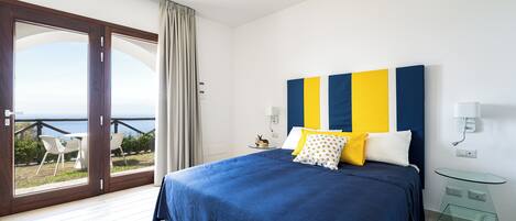 Un dormitorio con una cama grande, una mesita de vidrio y vista al mar a través de una puerta corrediza.
