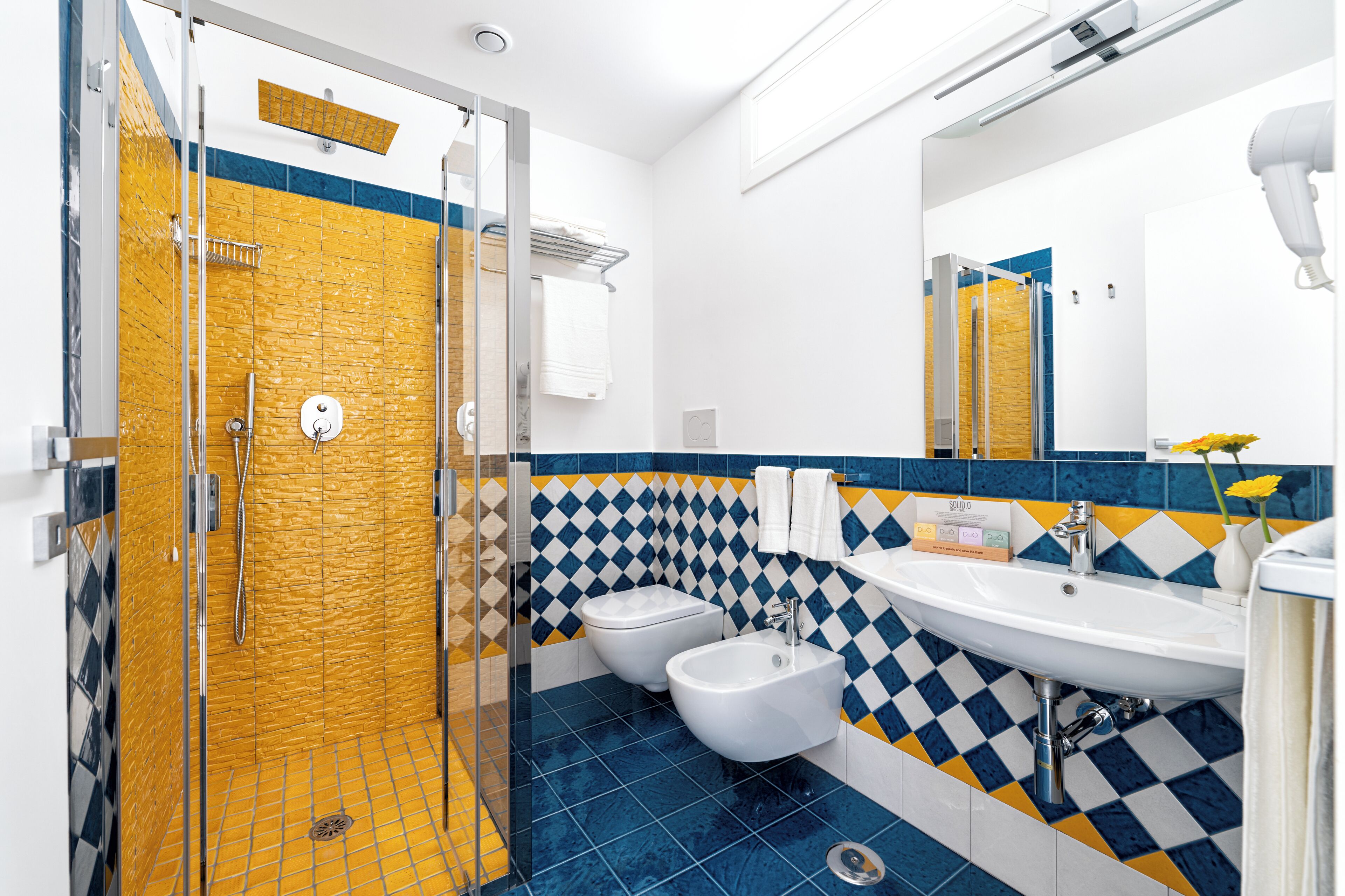 A bathroom with a shower, bidet, and sink, featuring a checkered tile pattern.