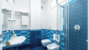 A modern bathroom with a sink, two toilets, a glass shower enclosure, and blue-tiled walls. - Tenuta dell'AlMa (Amalfi)