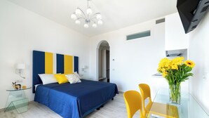 A modern bedroom with a bed, bedside tables, a glass table with chairs, a vase of flowers, and a TV. - Tenuta dell'AlMa (Amalfi)