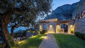 A stone building with a paved pathway leading to a wooden door, surrounded by greenery and overlooking a mountainous landscape. - Tenuta dell'AlMa (Amalfi)