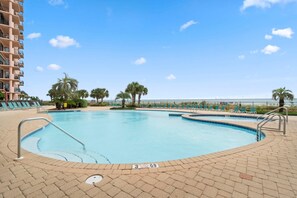 A swimming pool with lounge chairs, palm trees, and a high-rise building in the background.