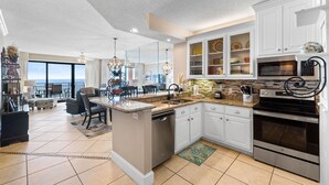 A modern kitchen with white cabinetry, a central island, stainless steel appliances, and a view to the outside. - Seachase 704w (Orange Beach)