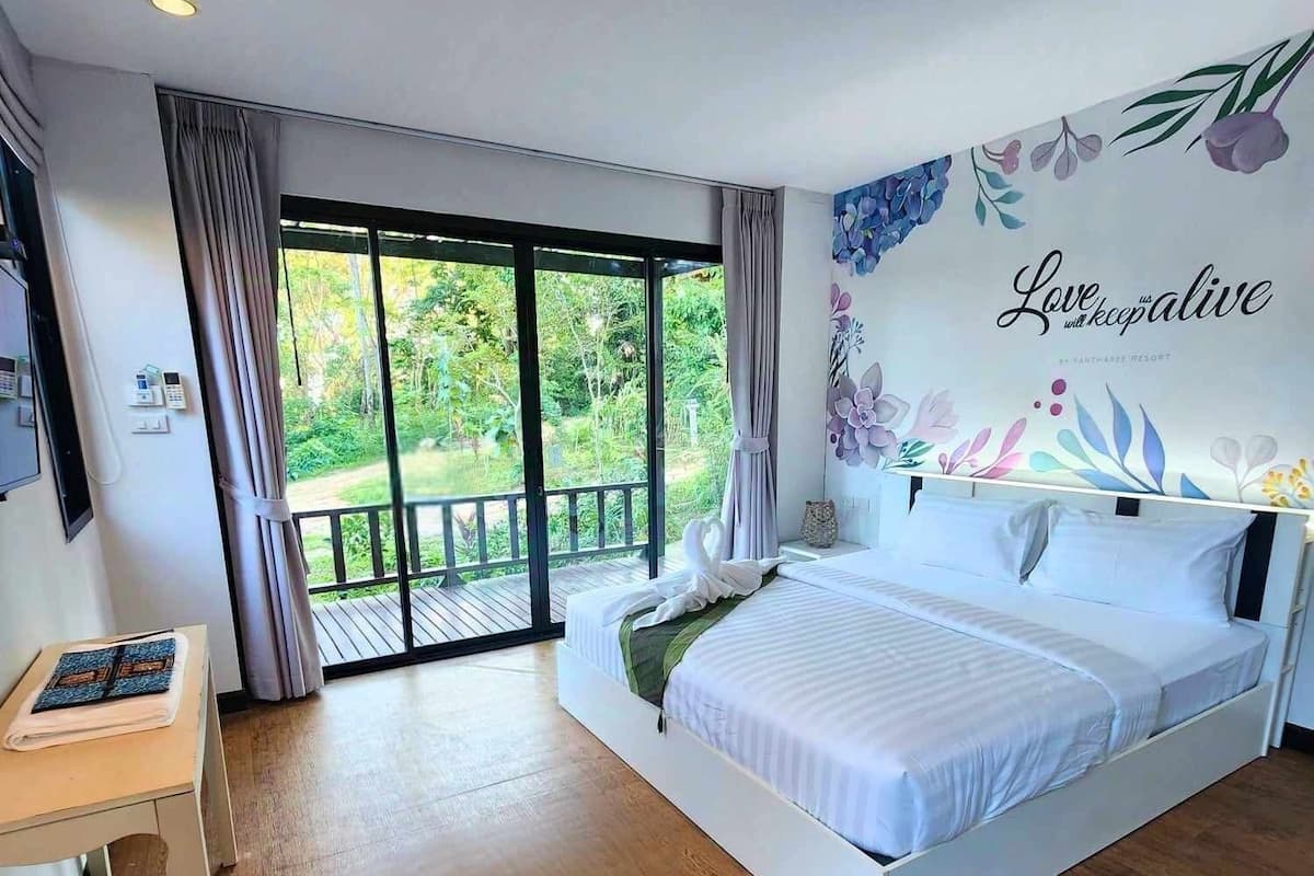 Une chambre avec un grand lit, un bureau et une porte-fenêtre coulissante donnant sur un balcon.