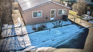 A small house with a sloped roof, a fenced yard, and snow on the ground.