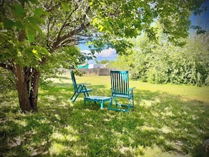 A grassy outdoor area with two blue chairs under a tree. - Vintage-Modern Adobe Escape 2 Bedroom 1 Bath (Antonito)