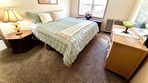 A bedroom with a bed, a nightstand, a lamp, a dresser, a window, and a picture on the wall.