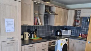 Una cocina compacta con armarios de madera, microondas, tetera y lavadora.