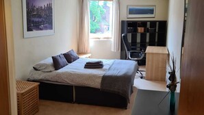 Un dormitorio con cama, escritorio, silla, ventana y puerta.
