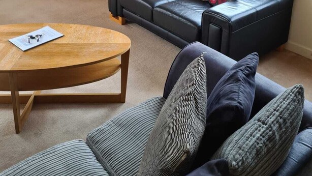 Un salón con un sofá de cuero negro, una mesa de centro de madera, un televisor y un ventanal con vistas a la ciudad.