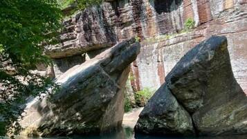Formación rocosa natural con grandes rocas parcialmente sumergidas en agua, rodeada de vegetación.