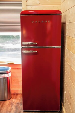 Un refrigerador Galanz rojo en una cocina con paredes de madera y un ventanal.