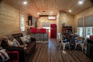 A cozy cabin interior with a wooden interior, a dining area with metal chairs, a red refrigerator, and a kitchen with a bar counter.