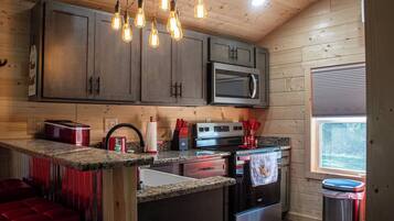 A kitchen with wooden cabinets, a microwave, a stove, and a trash can.