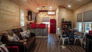 Een gezellig chaletinterieur met houten inrichting, een eethoek met witte stoelen, een rode koelkast en een keuken met een rode kookplaat.