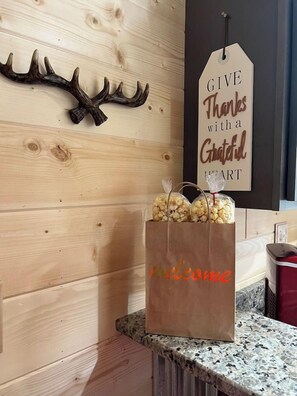 A wooden wall with a deer antler decoration and a 'GIVE Thanks with a Grateful Heart' sign. A brown paper bag with 'welcome' written on it is placed on a granite countertop.
