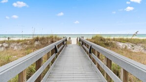 Une promenade en bois qui mène à une plage, avec un ciel dégagé.