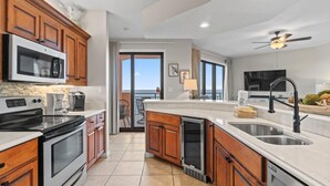 Une cuisine moderne avec des meubles en bois, des appareils en acier inoxydable, un grand îlot central doté d’un évier et une vue sur l’extérieur.