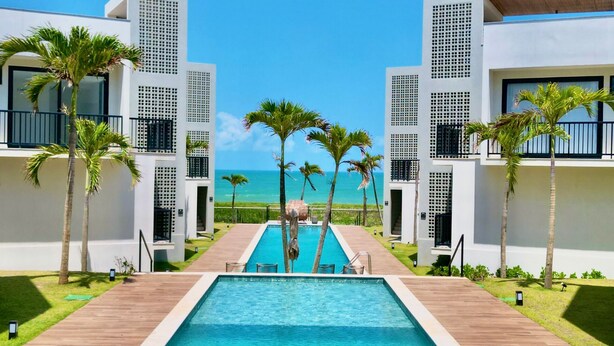 Un hôtel moderne doté d’une piscine centrale, de palmiers et offrant une vue sur l’océan.