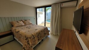 Une chambre avec un lit, un bureau en bois, une télévision et une porte-fenêtre coulissante donnant sur un balcon avec une piscine.