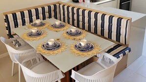 Un coin repas avec un banc à rayures, des chaises blanches et une table dressée avec des assiettes et des tasses.