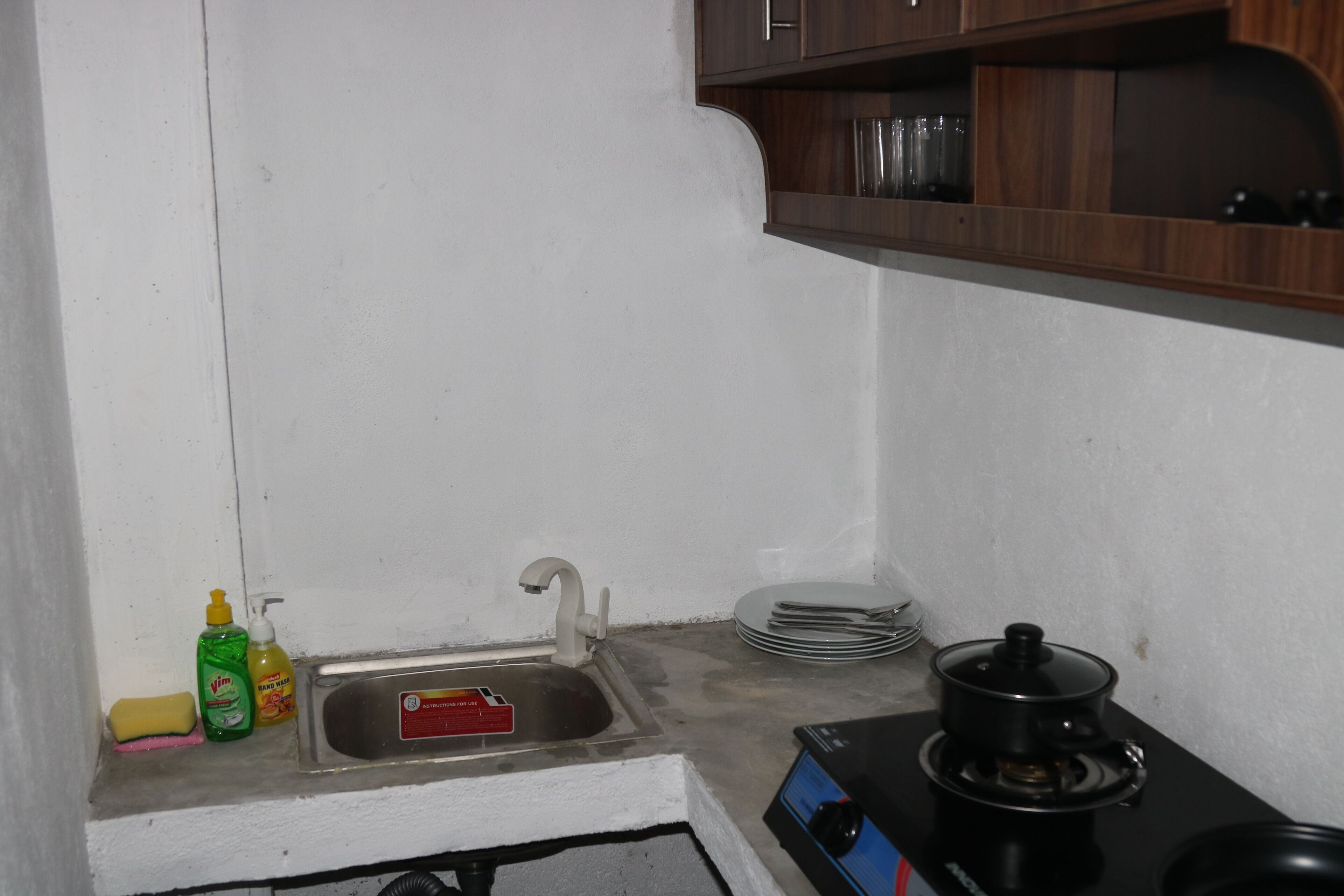 A small kitchen with a sink, a stove, and a shelf above the sink.