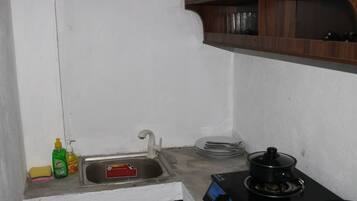 A small kitchen with a sink, a stove, and a shelf above the sink.
