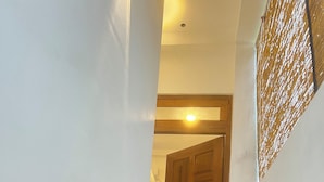 A hallway with a wooden door at the end, a white wall, and a light fixture on the ceiling. - The Villa Sea Breeze (Thalpe)
