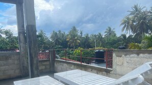 A rooftop terrace with white lounge chairs, a concrete wall, and a view of palm trees and a water tank. - The Villa Sea Breeze (Thalpe)