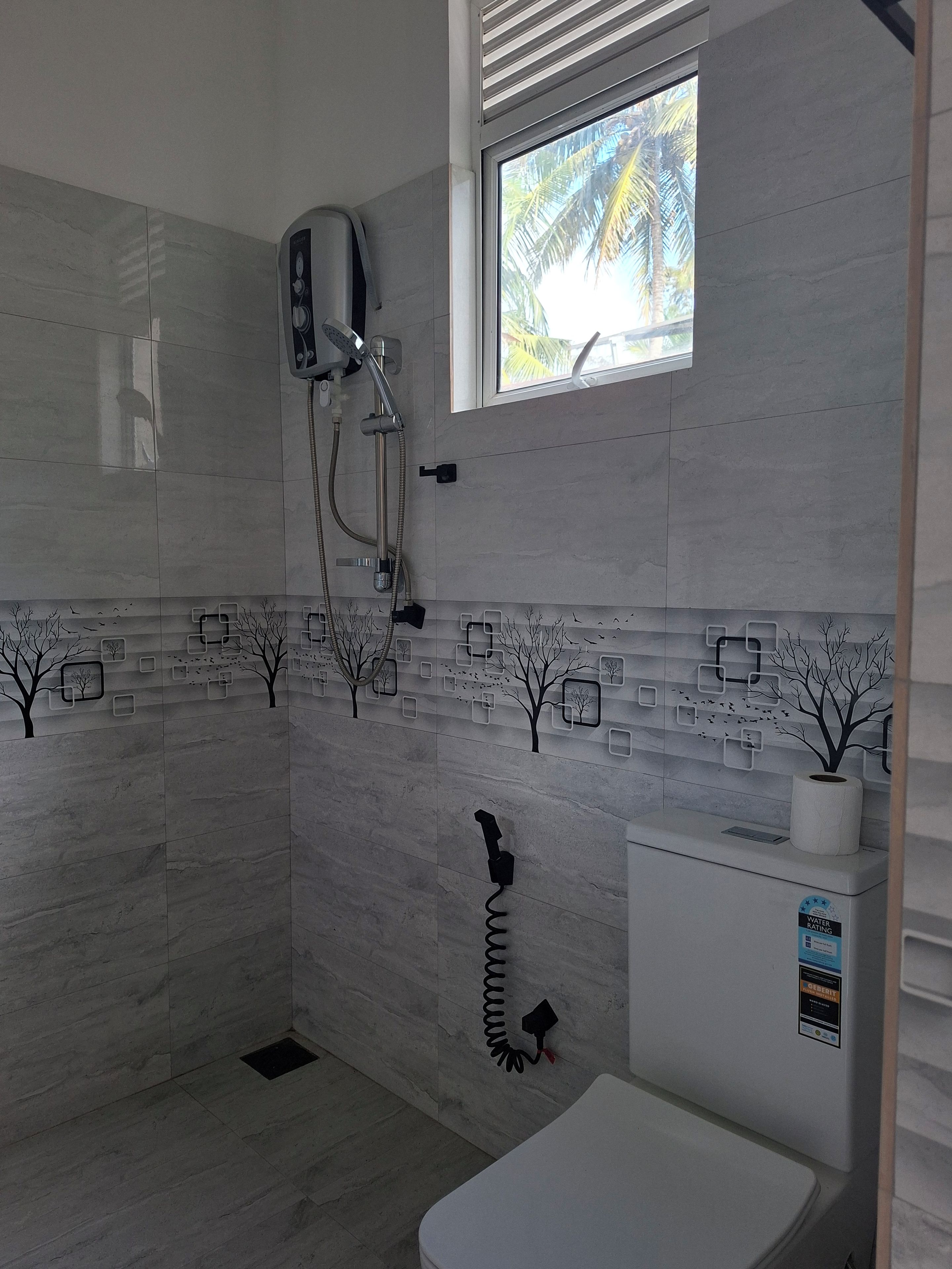 Un baño con ducha, inodoro y ventana con vista a palmeras.