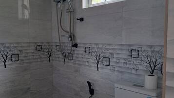 Un baño con ducha, inodoro y ventana con vista a palmeras.