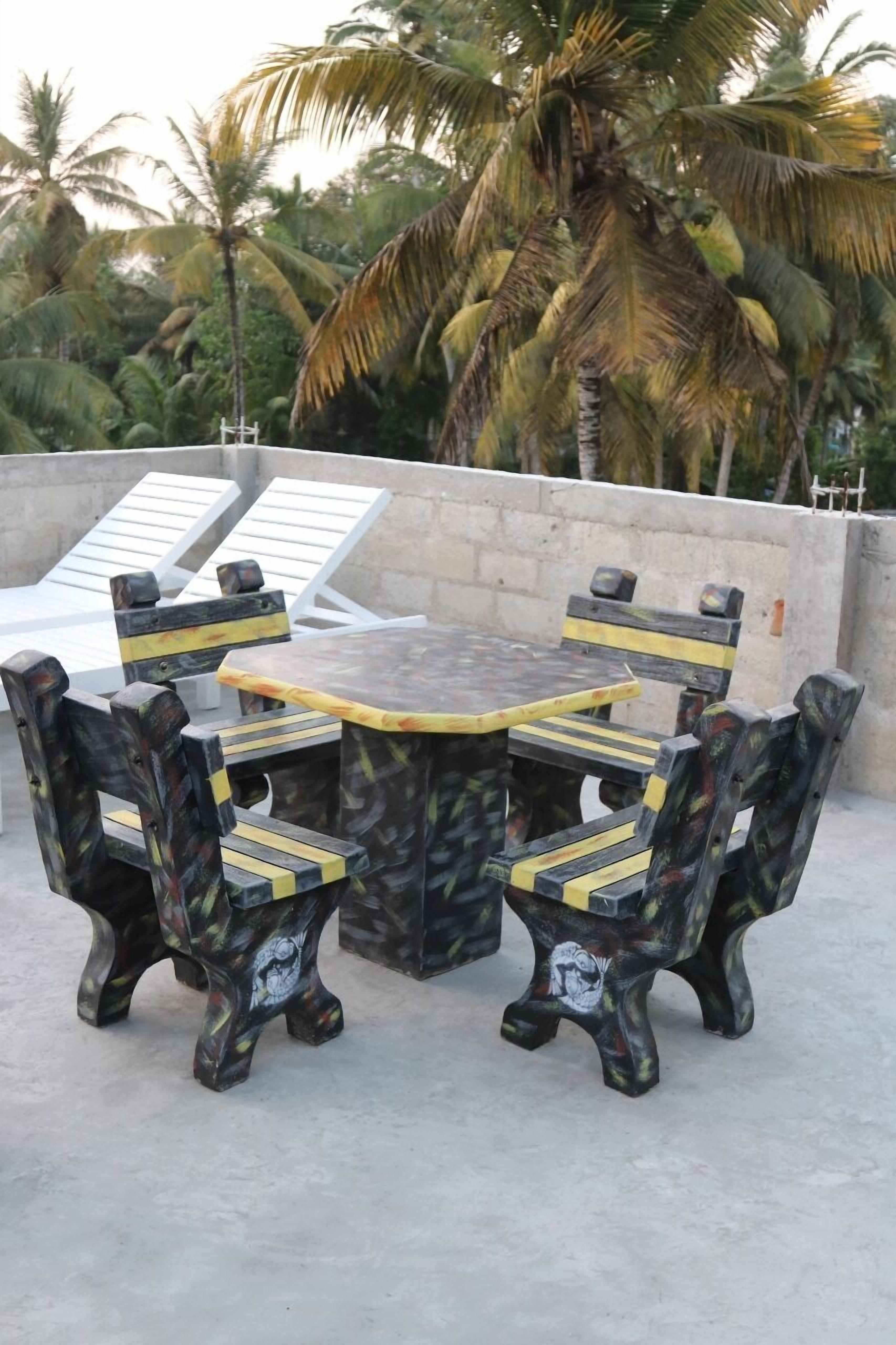 A round outdoor table with chairs, surrounded by a concrete wall and palm trees.