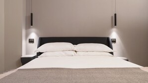 Quarto moderno com cama, mesas de cabeceira e luminárias pendentes.