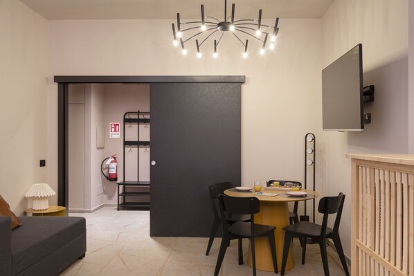 A modern room with a dining area, a sofa, a TV mounted on the wall, and a chandelier.