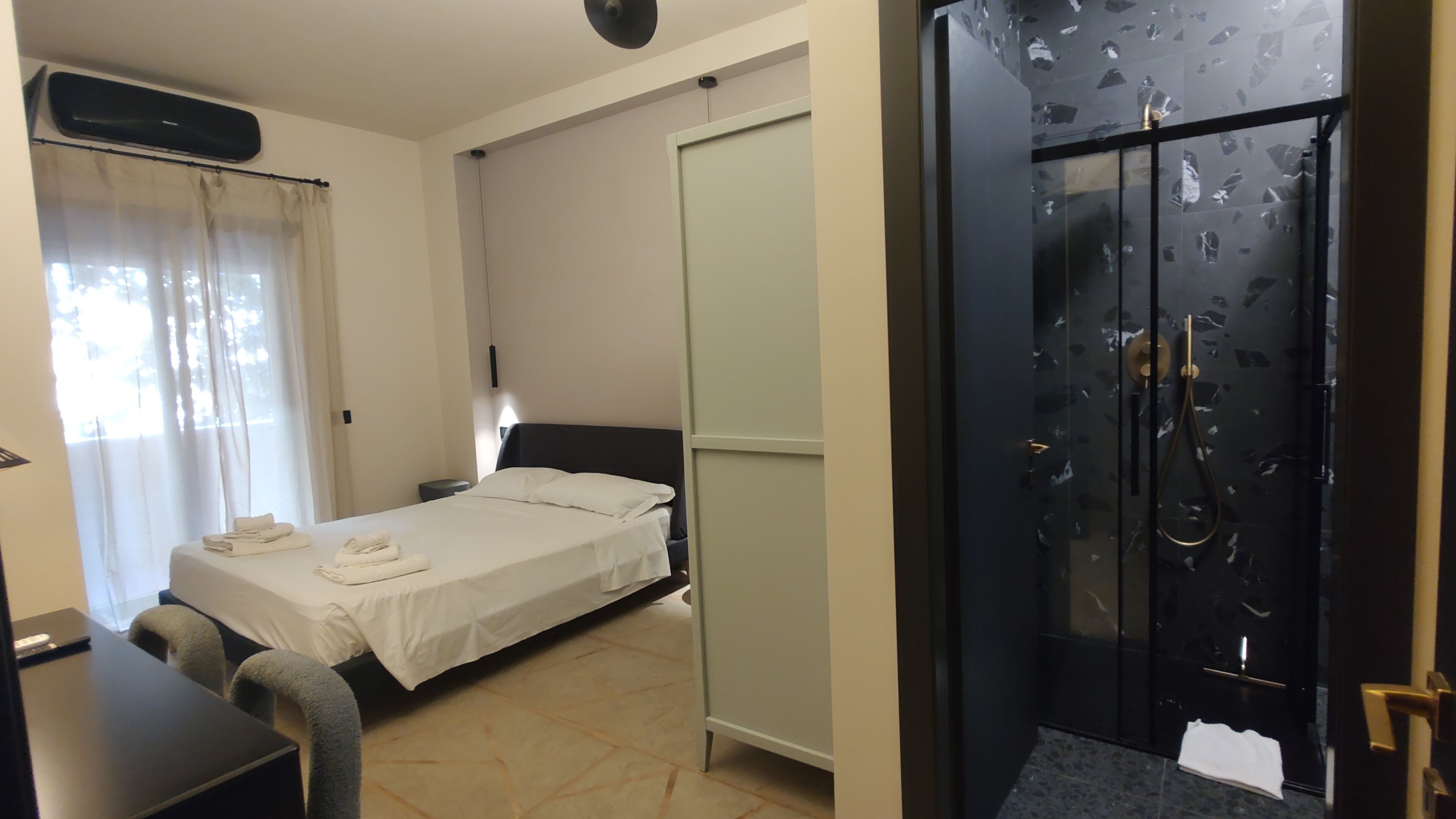 A hotel room with a bed, a desk, a wardrobe, and a shower area.