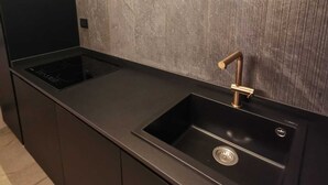 Uma cozinha moderna com bancada preta, pia embutida com torneira dourada e revestimento de parede com padrão texturizado.