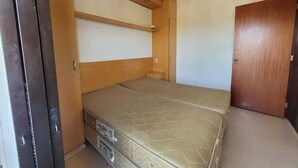 A compact bedroom with a single bed, built-in storage, a ceiling fan, and a door.