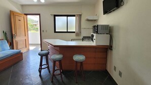 A compact kitchen with a microwave, a small island with stools, a ceiling fan, and a TV mounted on the wall.