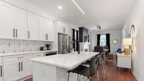 A modern kitchen with white cabinetry, a marble island, and a dining area with bar stools. - Spacious 4-bedroom house in charming Richmond with WiFi and AC (Richmond)