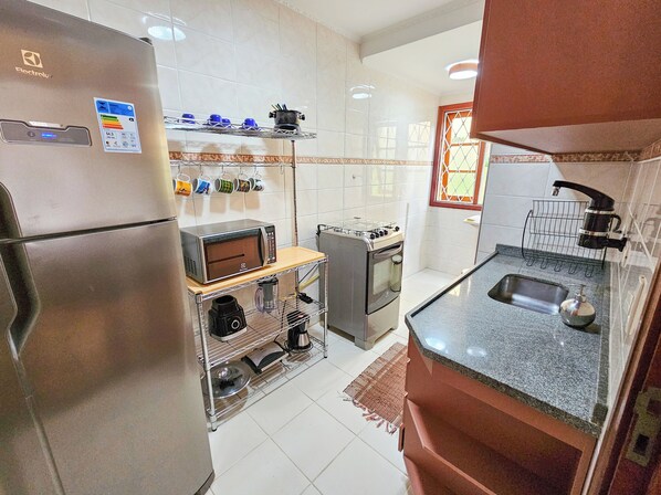A compact kitchen with a refrigerator, microwave, stove, and sink. - Apartamento Alto Alto da Boa Vista (Campos do Jordão)