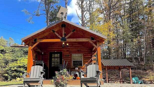 Een rustieke chalet met een houten gevel, een veranda met twee stoelen en een klein overdekt gedeelte met een tafel en stoelen.