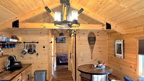 Een gezellig blokhutinterieur met een houten plafond, een eethoek met een ronde tafel, een keuken met houten kastjes en een woonkamer met een bank.