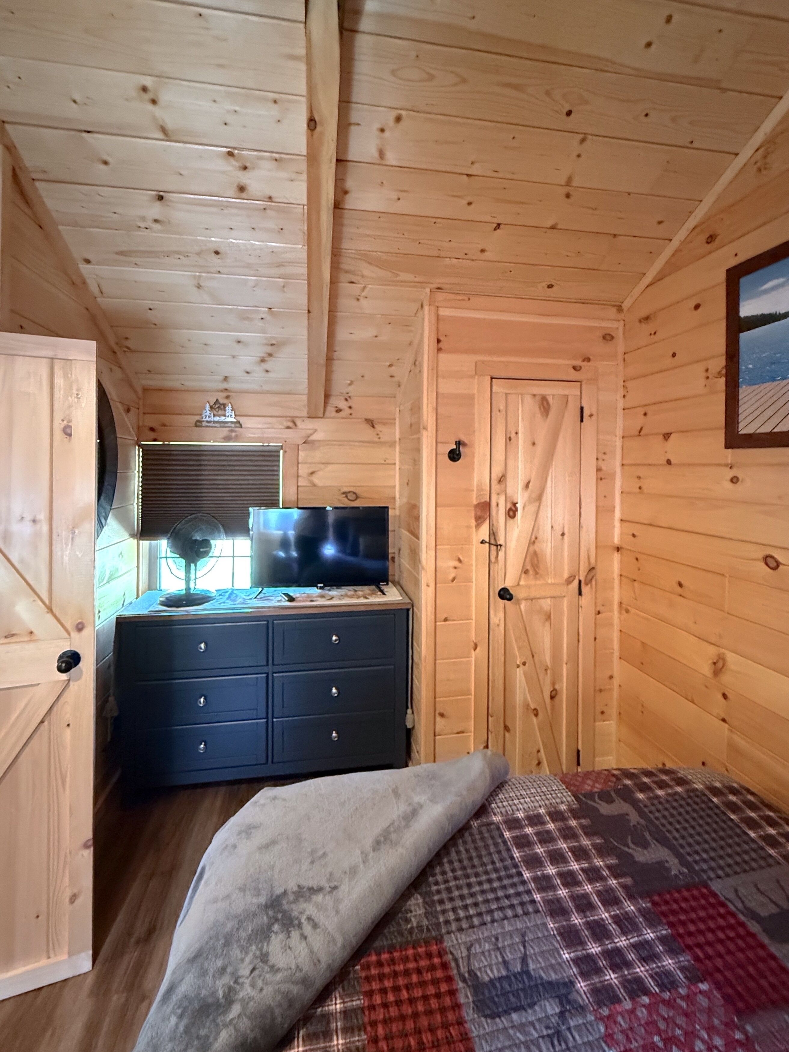 Una stanza in legno arredata con un letto, una cassettiera, una televisione e una porta.