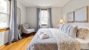 A hotel room with a bed, a chair, a lamp, and two paintings on the wall.