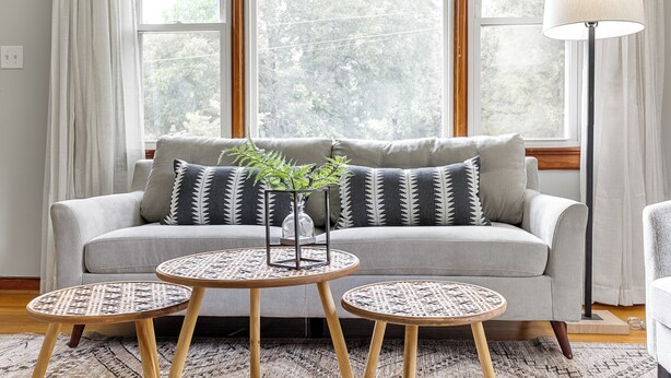 A living room with a grey sofa, two round tables with woven tops, and a floor lamp.